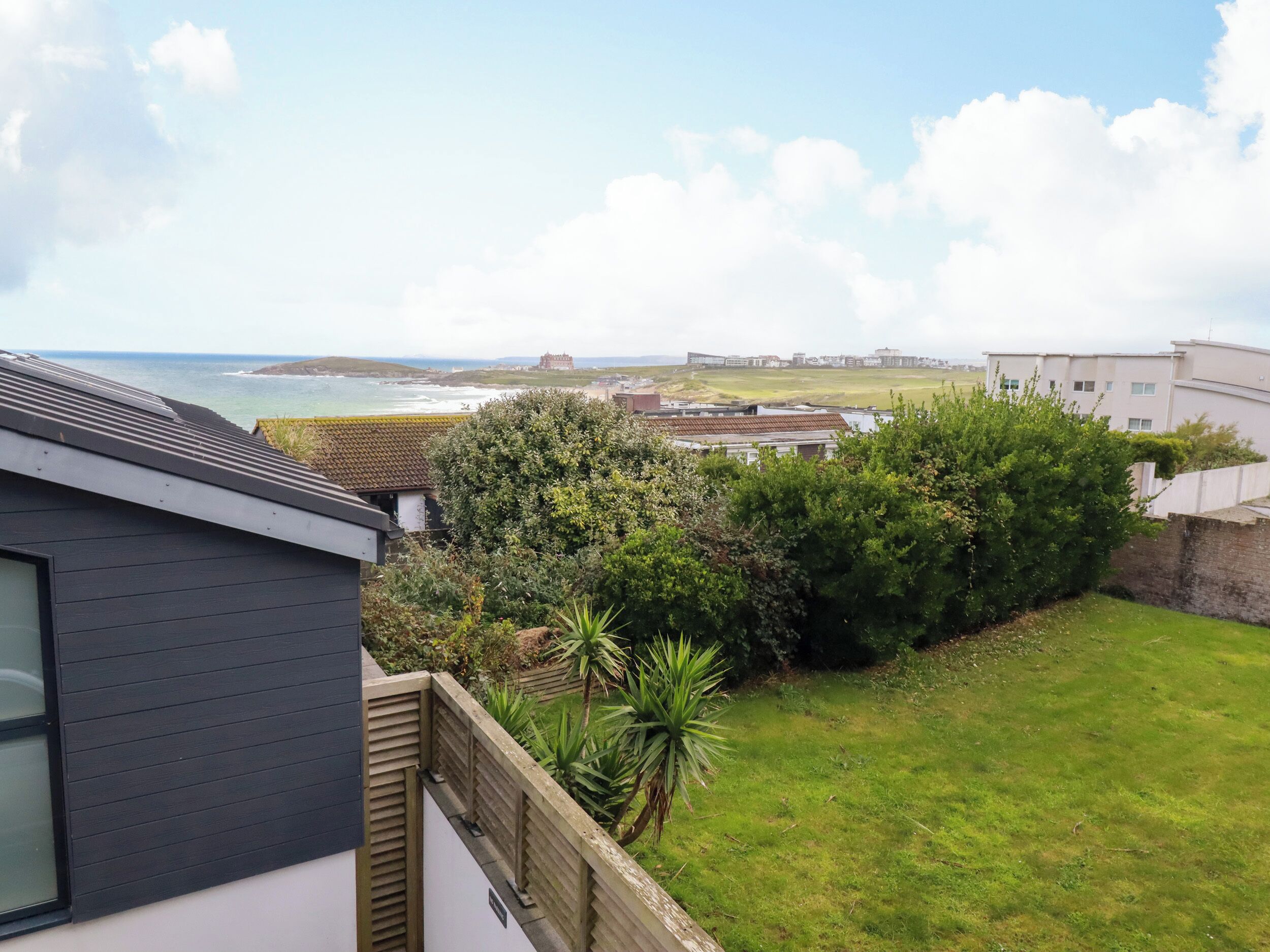 A residential area with a view of the sea, a grassy lawn, and a building with a tiled roof.