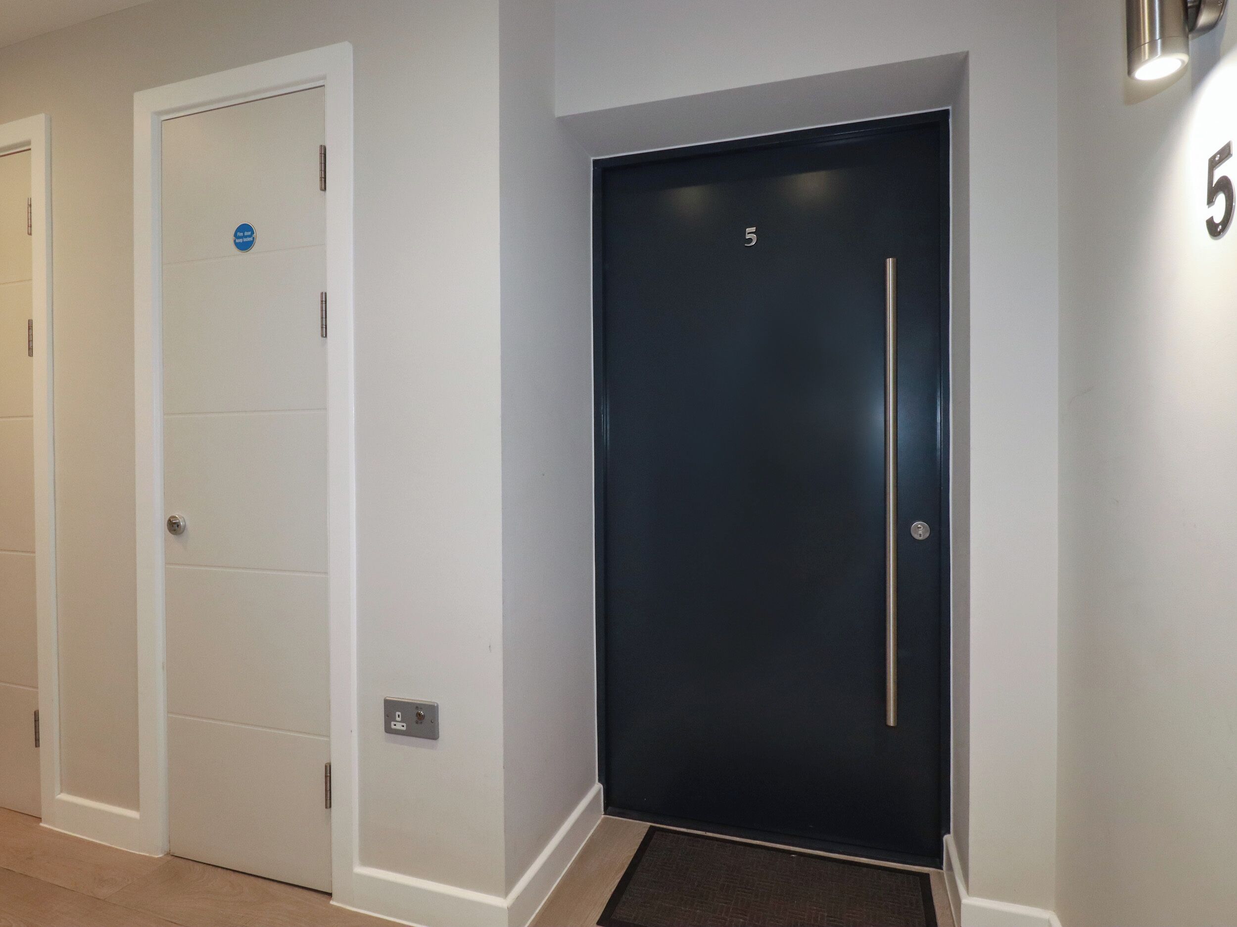 A hallway with two doors, one white and one black, with a number 5 on the wall.