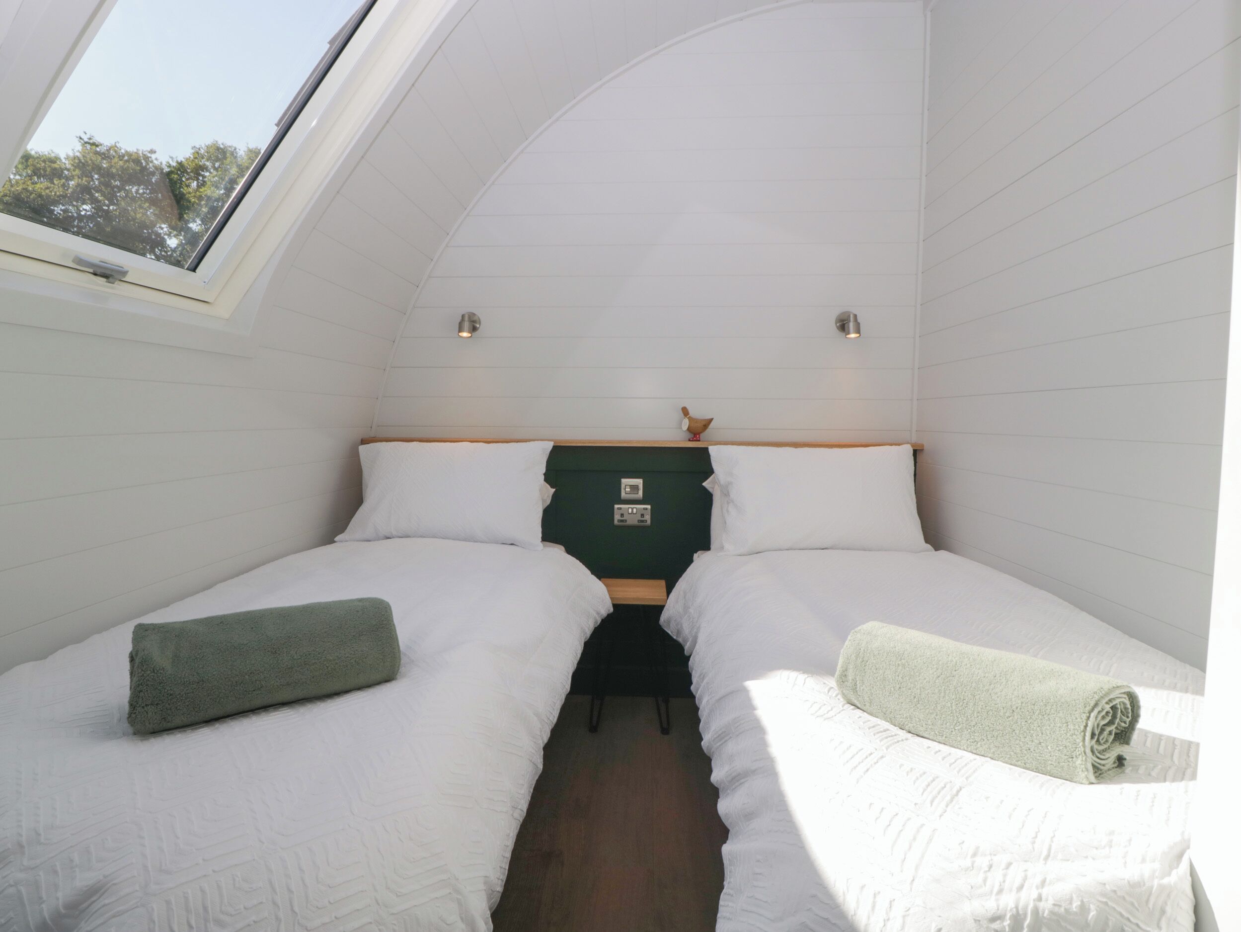 Una habitación pequeña y acogedora con dos camas, un tragaluz y una pared verde.