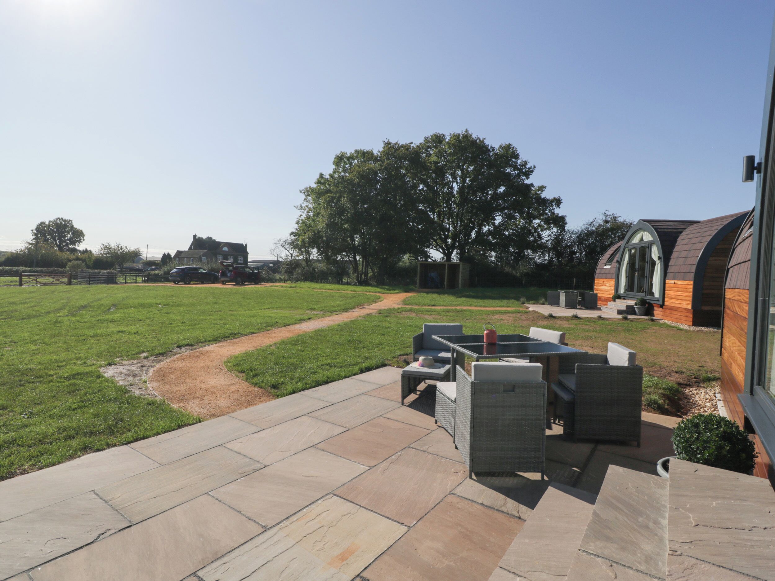 Un espace patio aménagé avec du mobilier d’extérieur et un chemin de pierres menant à un champ d’herbe.
