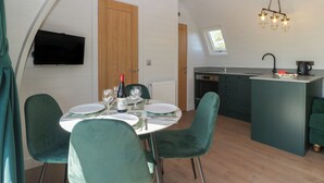 A dining area with a table set for four, a kitchen with a sink and stove, and a television mounted on the wall. - Leadon View Willow (Newent)