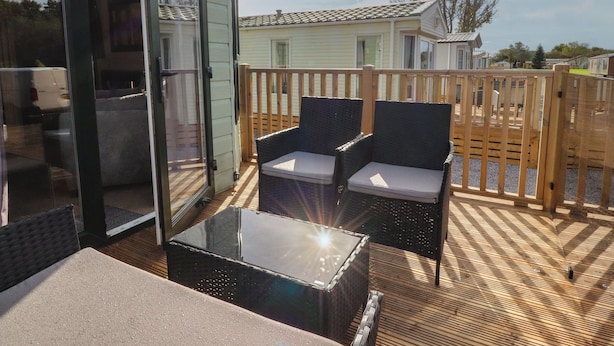 A deck with wicker chairs and a glass-top table, wooden deck flooring, and a view of a house in the background. - Ashcroft (Preston)