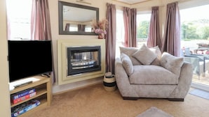 A living room with a flat-screen TV, a fireplace, a sofa, and a large window with curtains. - Ashcroft (Preston)