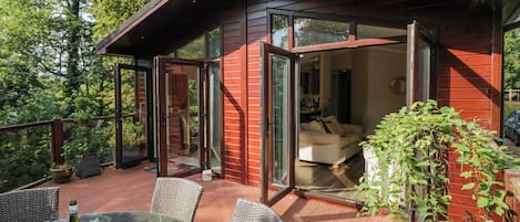 Una casa moderna con una terraza, puertas de cristal que dan a una sala de estar y una mesa con copas de vino.