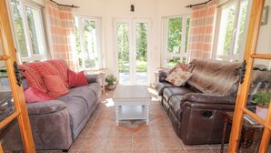 A cozy living room with two sofas, a coffee table, and a view of the outdoors through large windows. - Mill House (Moville)