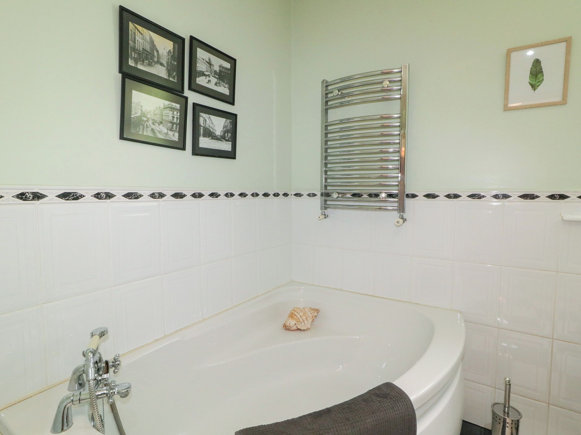 A bathroom with a bathtub, a towel rack, and four framed pictures on the wall.
