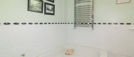 A bathroom with a bathtub, a towel rack, and four framed pictures on the wall.