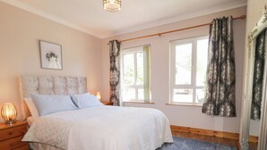 A bedroom with a bed, bedside lamps, a wooden nightstand, a mirror, and a window with curtains. - Mill House (Moville)
