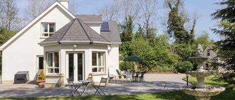 Een tweelaags huis met een patio, buitenmeubels en een tuin met een fontein.