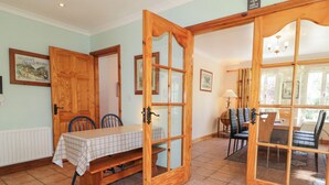 A dining area with a wooden table and chairs, a checkered tablecloth, and a wooden door leading to another room. - Mill House (Moville)