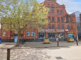 Un edificio de ladrillo rojo con un letrero que dice "BREWERS QUAY" y un cartel de "Se vende".