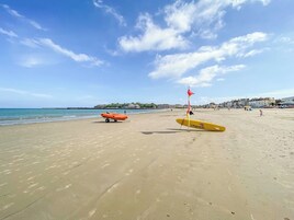 Una playa con equipo de salvavidas, incluyendo una bandera roja y una tabla de surf amarilla.