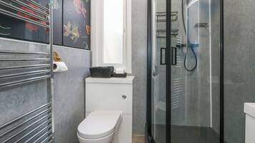 Un baño moderno con inodoro, cabina de ducha de vidrio y un perchero para toallas.