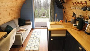 A cozy cabin interior with a wooden interior, a sofa, a small kitchen area, and a view of the outdoors. - Hobhole (Spilsby)