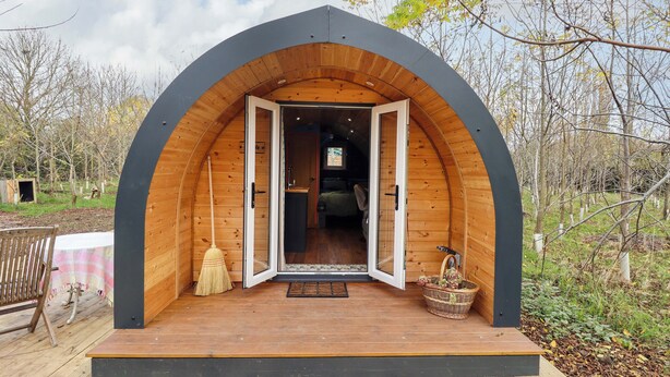 A wooden arched structure with a wooden deck leading to an open door, surrounded by trees. - Hobhole (Spilsby)