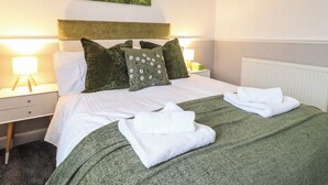 A neatly made bed with green bedding, two pillows, and a forest-themed wall hanging. - Charleston Cottage (Bridport)
