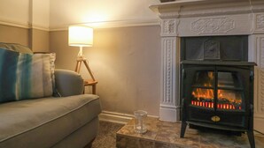 A cozy living room with a sofa, a standing lamp, and a fireplace. - Charleston Cottage (Bridport)
