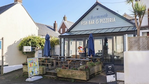 A fish bar and pizzeria with outdoor seating and a signboard advertising its offerings. - Charleston Cottage (Bridport)
