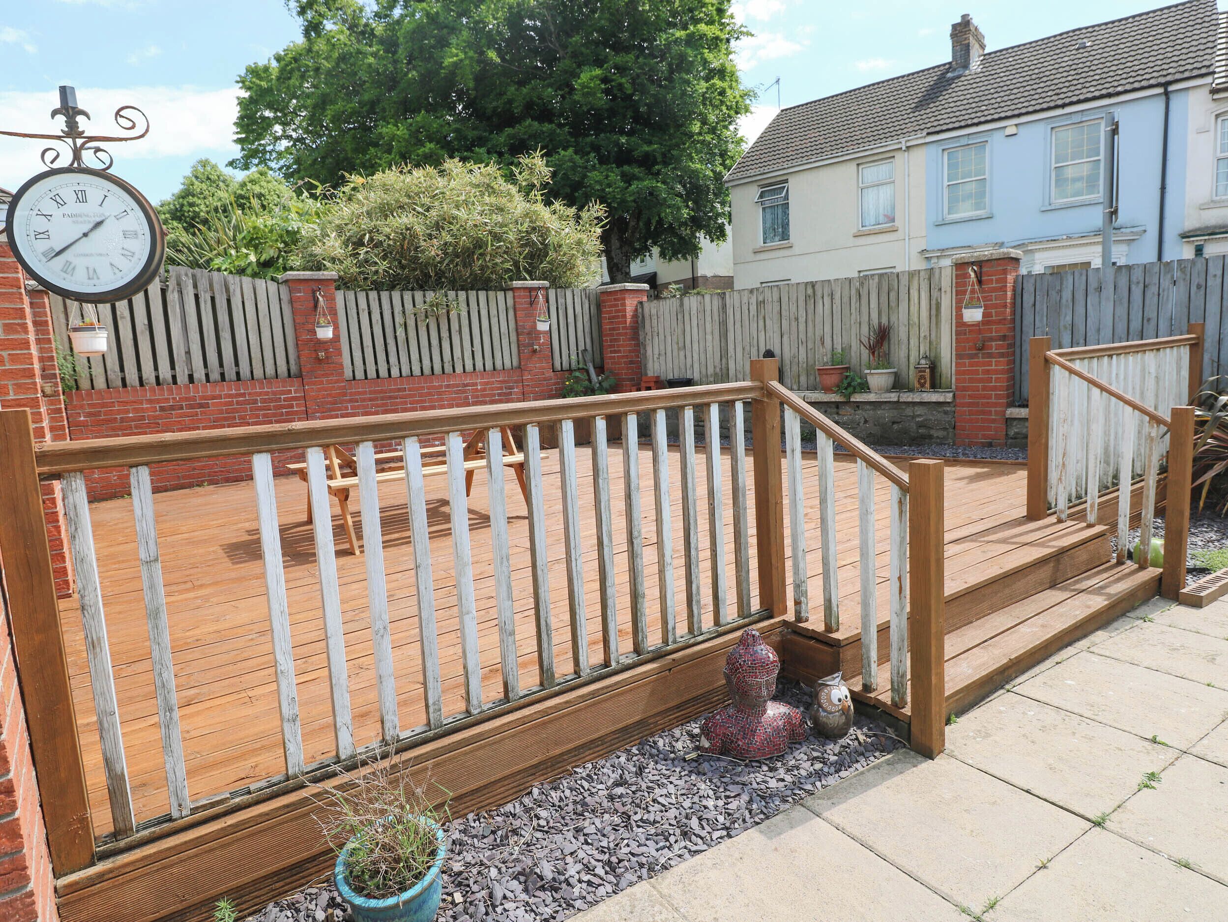 Une terrasse en bois avec une balustrade blanche, un mur en briques et une horloge.