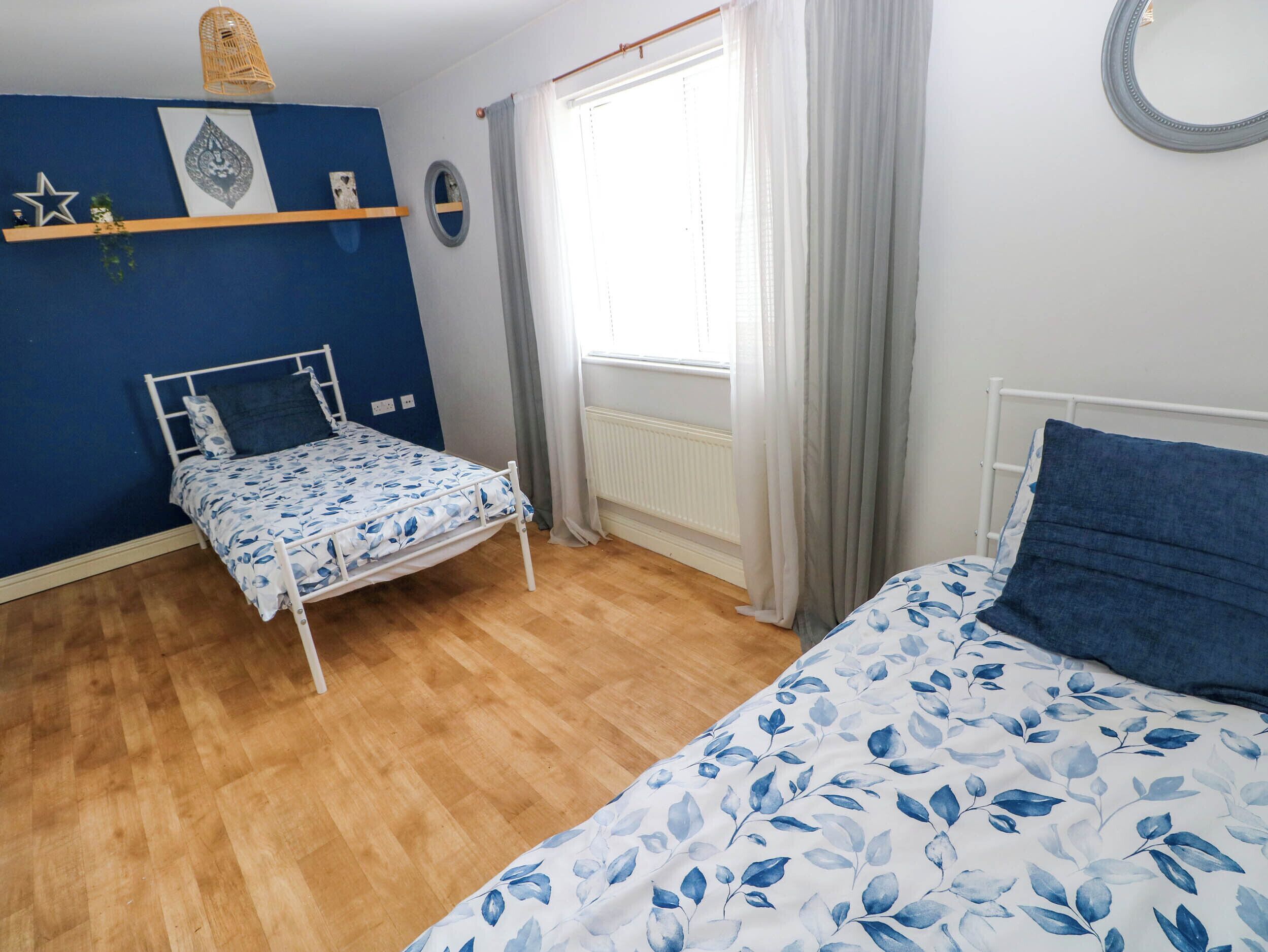 Quarto com duas camas, janela com cortinas, radiador e decorações nas paredes.