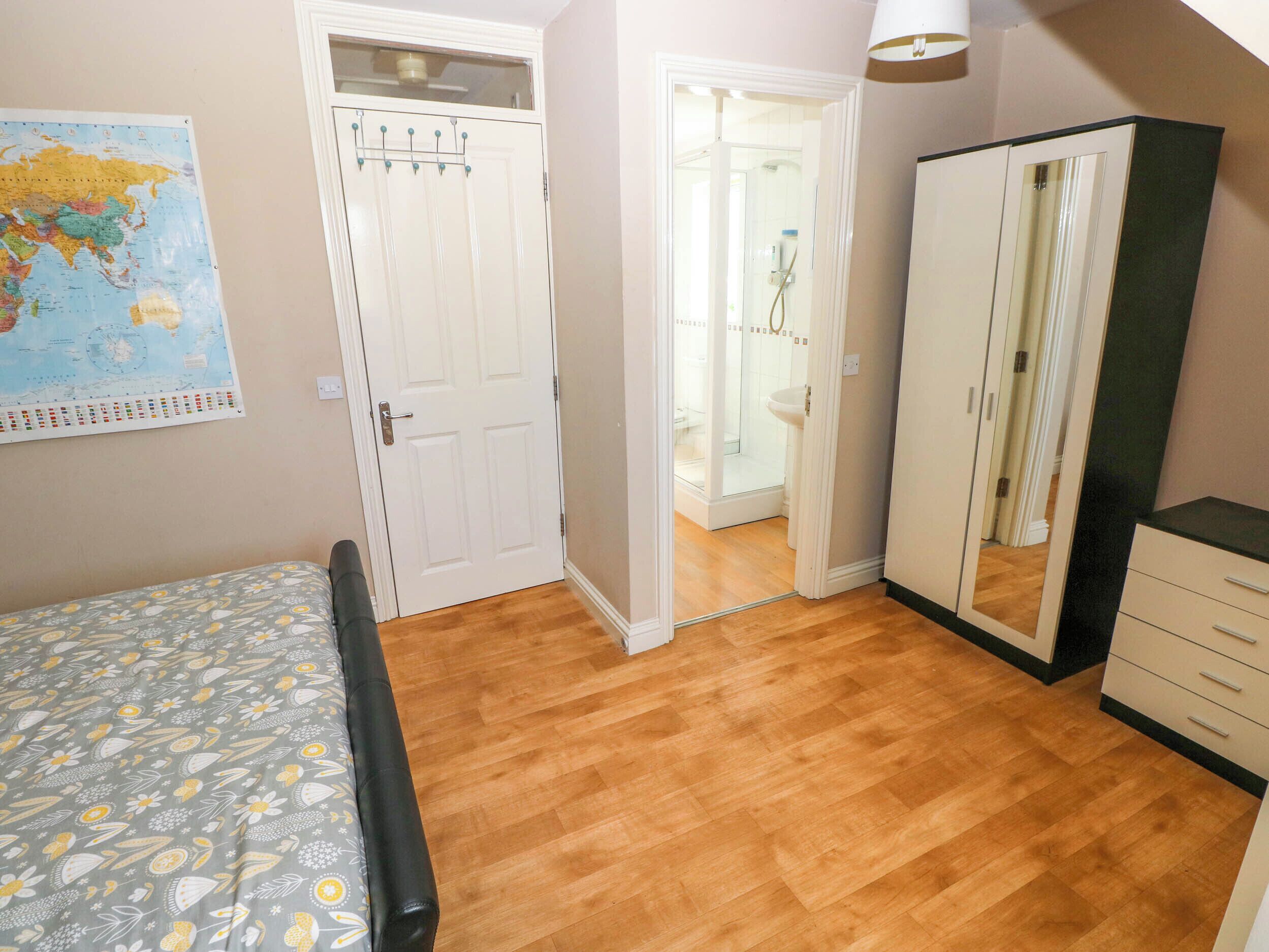A bedroom with a bed, a wardrobe, a bathroom with a shower, and a map on the wall.