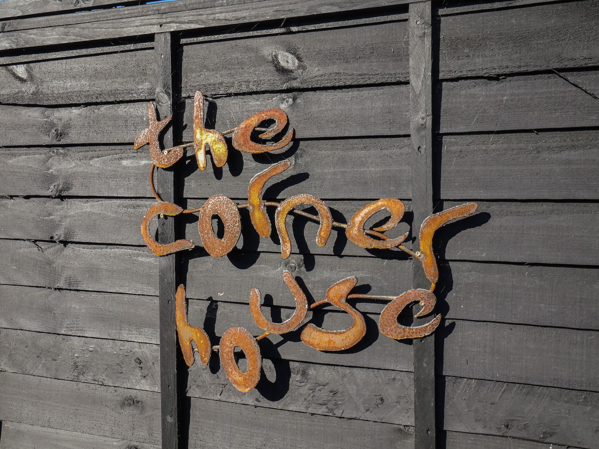 A rustic wooden wall with a decorative metal sign spelling "the corner house".