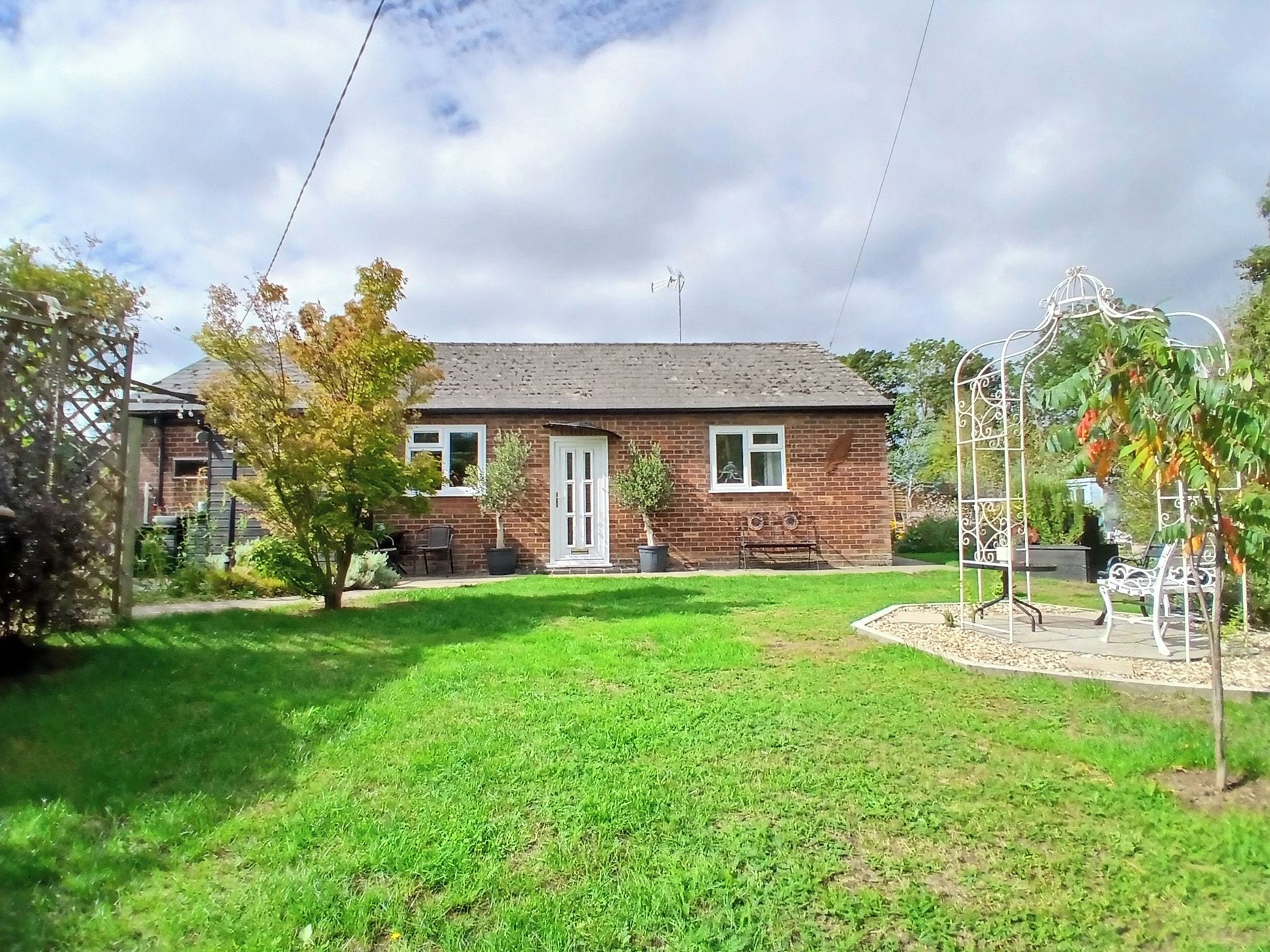 A brick house with a front door, a small front yard, and a metal garden structure.