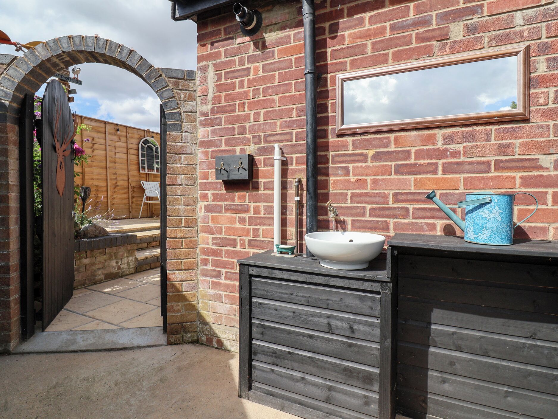 A rustic bathroom with a wooden bench, a white sink, and a blue watering can.