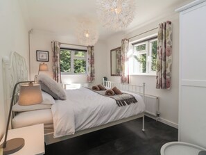 A bedroom with a bed, bedside lamp, window with curtains, radiator, and a ceiling light fixture. - The Corner House (Woodbridge)