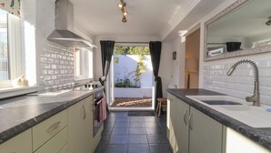 Cocina estrecha con estufa, lavamanos y armarios. Se ve una ventana con cortinas y vistas al exterior.