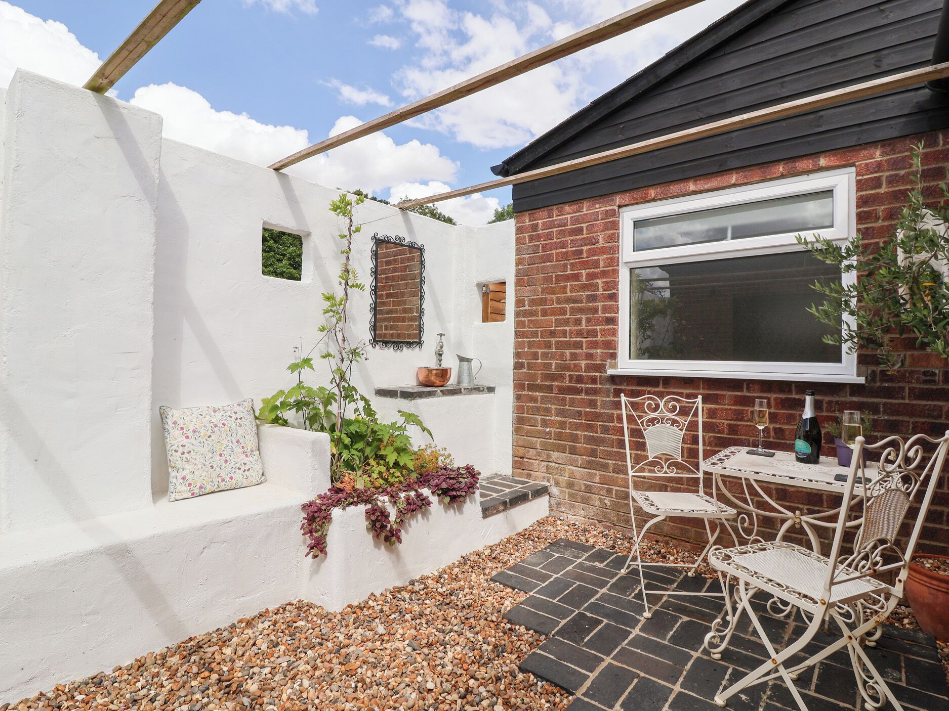 Une terrasse avec un mur blanc, un mur en briques, une fenêtre et une table avec des chaises.