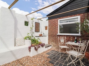 A patio with a white wall, a brick wall, a window, and a table with chairs. - The Corner House (Woodbridge)