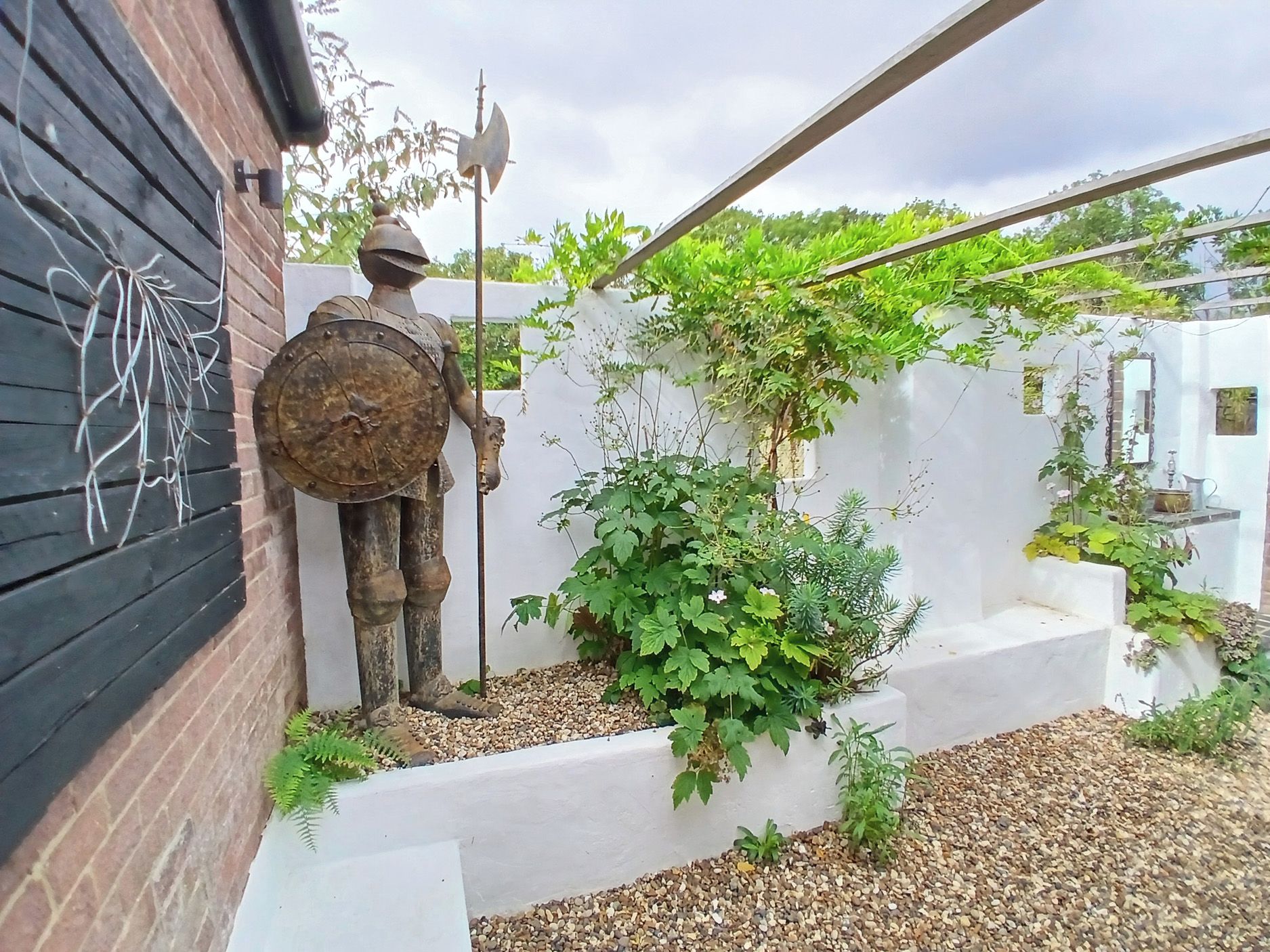 A statue of a soldier with a shield and spear, a white wall with greenery, and a wooden fence.