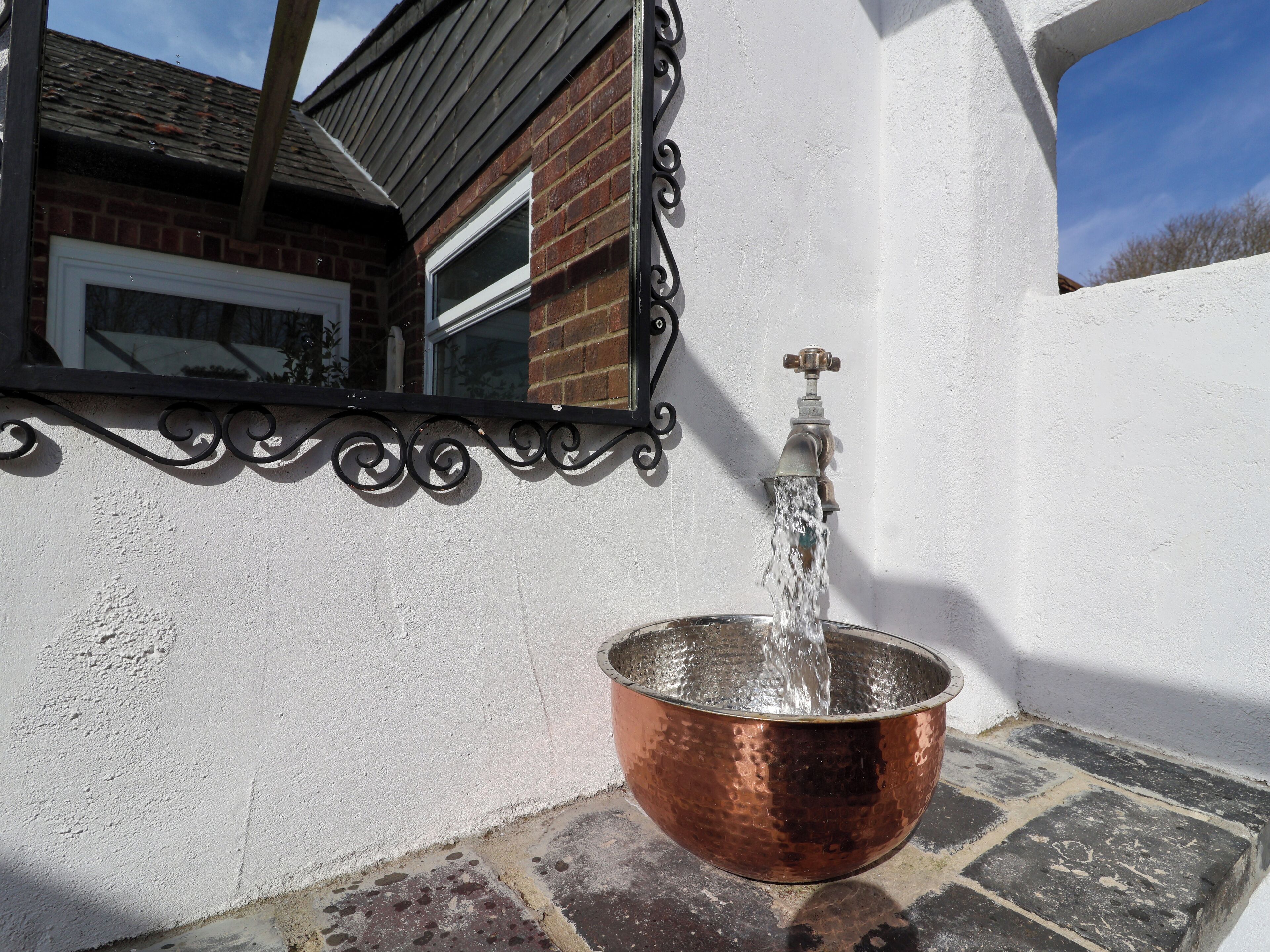 A copper basin under a wall-mounted tap with water flowing into it.