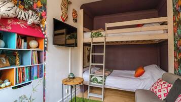 A bunk bed room with a bookshelf, a small table, and a green rug.