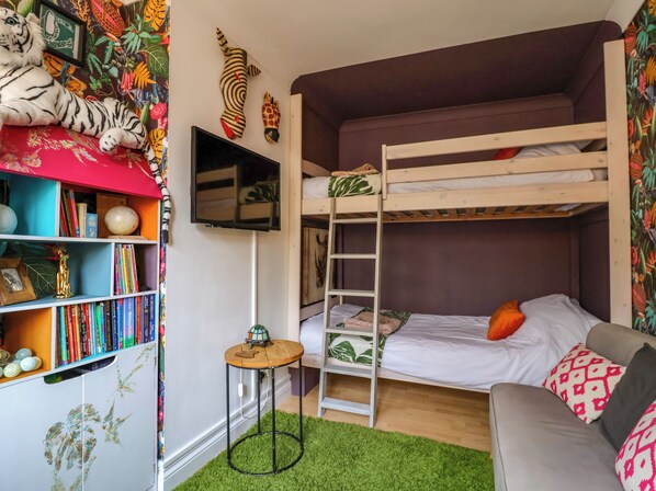 Habitación con literas, una estantería, una mesita pequeña y una alfombra verde.