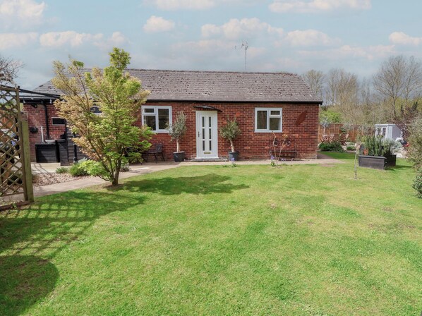 A brick house with a front door, windows, and a small garden with grass and plants. - The Corner House (Woodbridge)