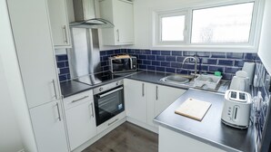 A modern kitchen with white cabinets, a stainless steel range hood, a built-in microwave, a double sink, and a window above the sink. - 104 The Laurels (Skegness)