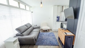 A compact living space with a sofa, a chair, a small wooden table, a television, and a kitchen area. - 104 The Laurels (Skegness)