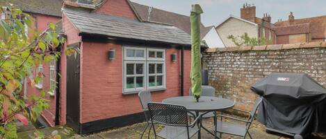A patio with a table and chairs, a barbecue grill, and a brick wall.