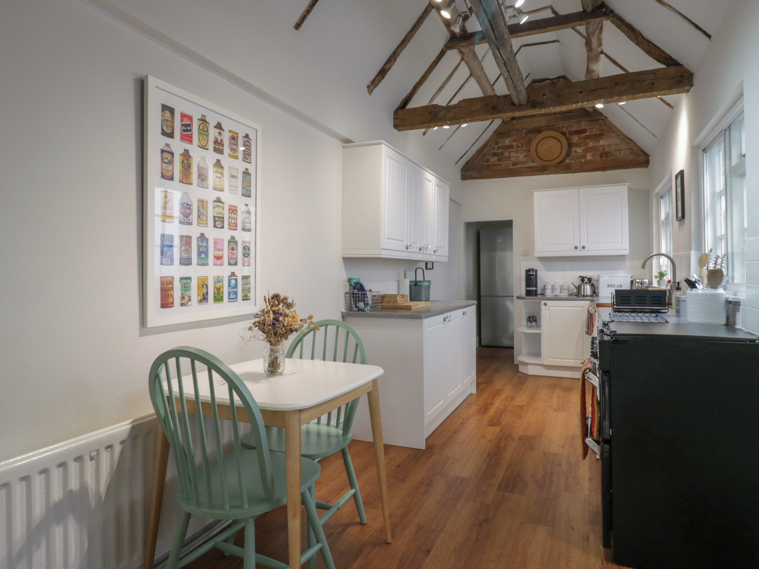 A modern kitchen with white cabinetry, a wooden ceiling, and a dining area with green chairs.
