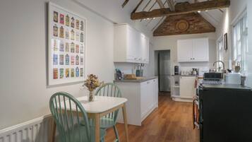 A modern kitchen with white cabinetry, a wooden ceiling, and a dining area with green chairs.