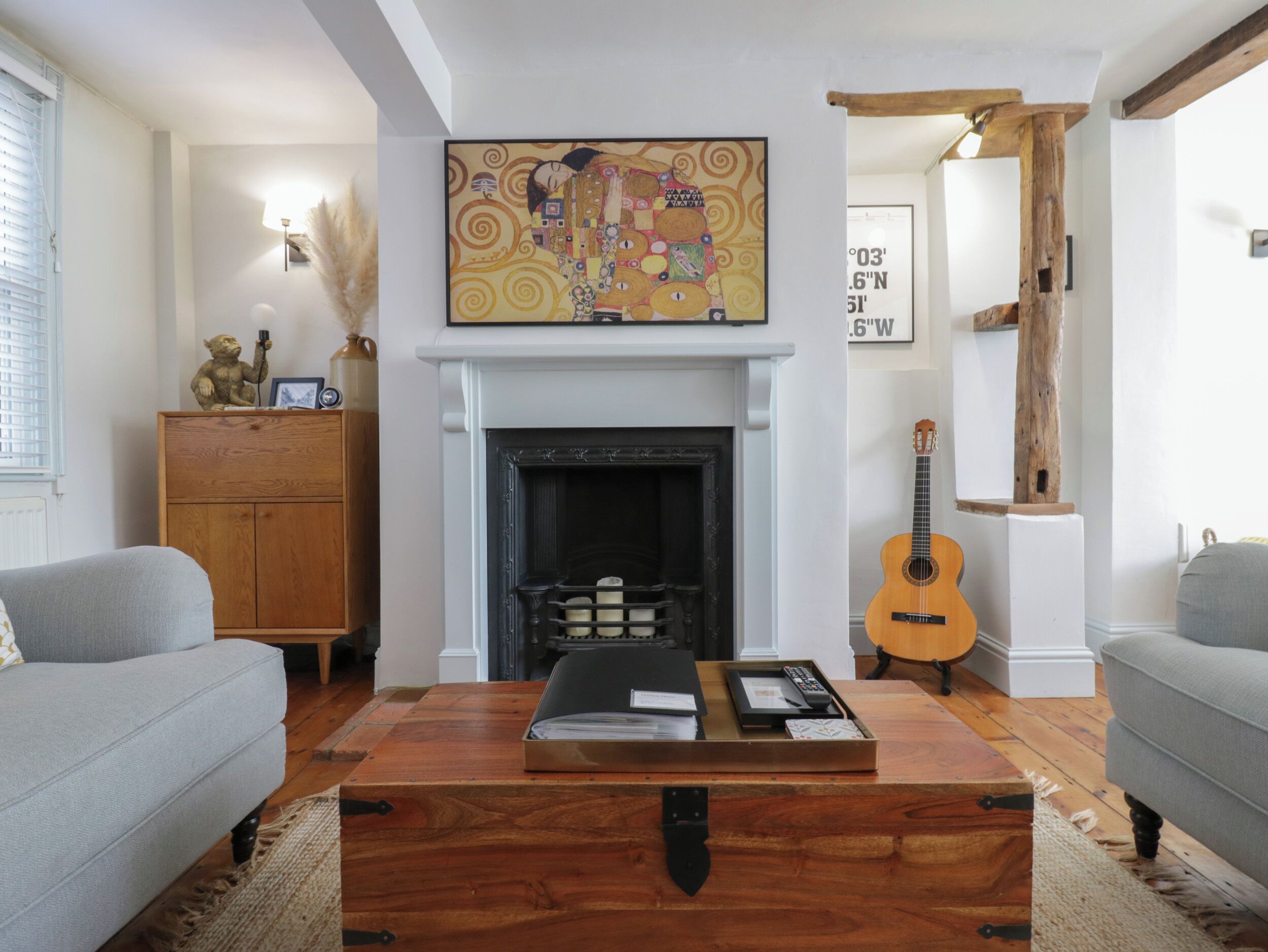 Una sala de estar con chimenea, un cuadro colgado, un aparador de madera, una guitarra y una mesa de centro con una bandeja.