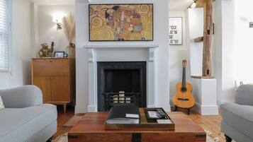 Una sala de estar con chimenea, un cuadro colgado, un aparador de madera, una guitarra y una mesa de centro con una bandeja.