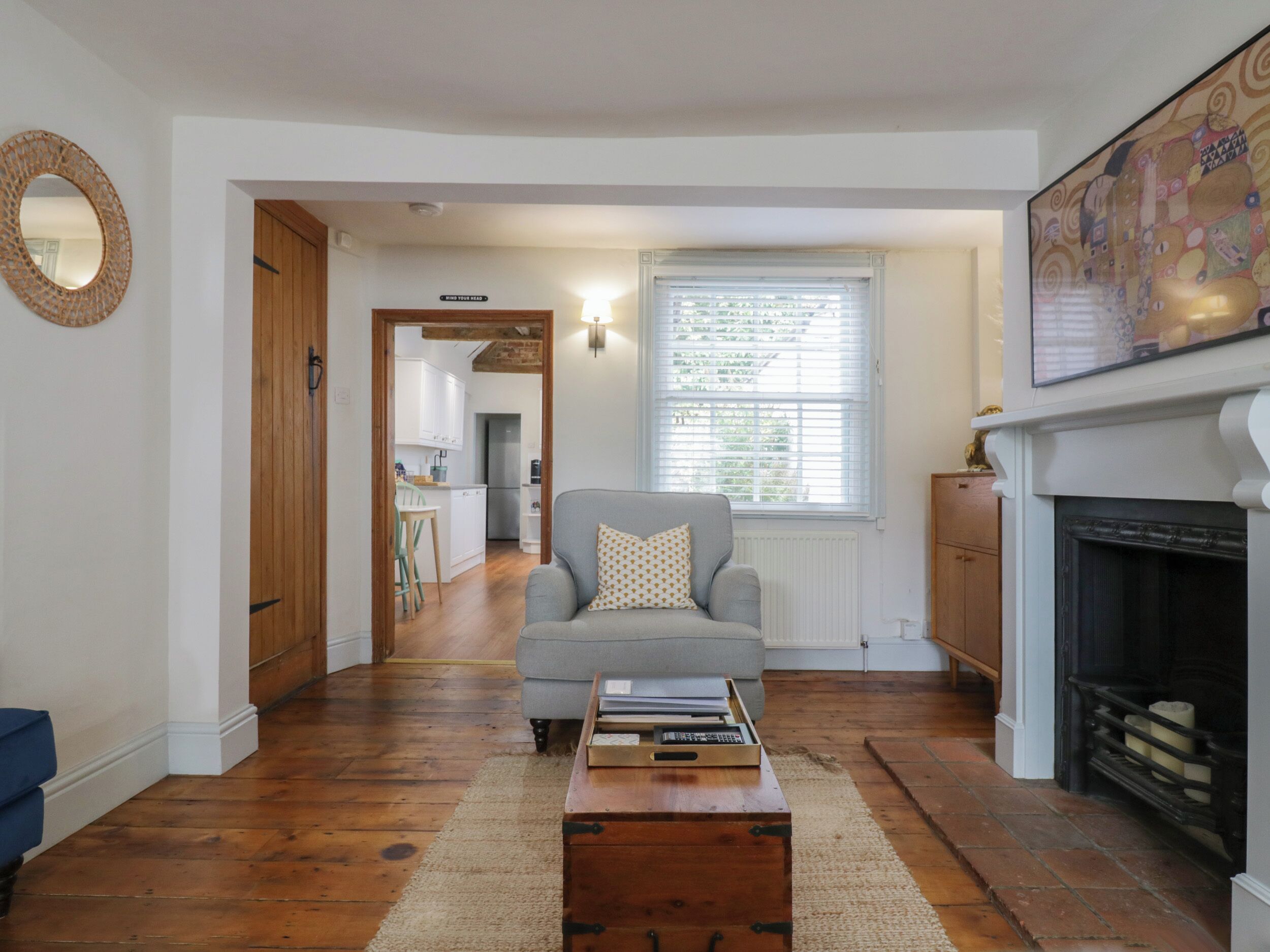 A living room with a sofa, a coffee table, a fireplace, and a kitchen visible through an open door.
