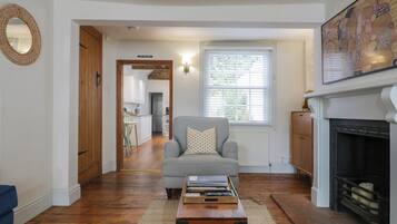 A living room with a sofa, a coffee table, a fireplace, and a kitchen visible through an open door.