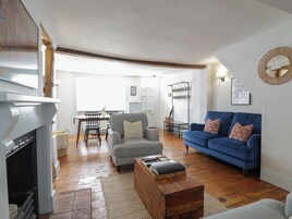 A living room with a fireplace, a blue sofa, a wooden coffee table, and a dining area in the background.