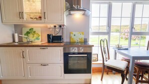 A kitchen with a built-in oven, a dining table with chairs, and a window with a view of the outdoors. - Thomond Hill (Naran)