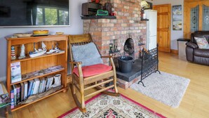 A cozy living room with a brick fireplace, wooden furniture, a bookshelf, and a television. - Thomond Hill (Naran)