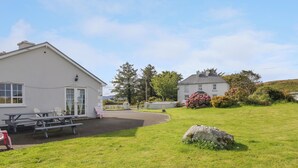 A white building with a patio area, outdoor seating, and a large rock in the foreground. - Thomond Hill (Naran)